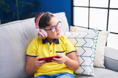 Adorable hispanic boy playing video game sitting on sofa at home