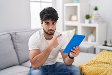 Sakallı İspanyol bir adam kanepeye oturmuş elini kaldırarak reklamını yapıyor, ciddi ve sakin bir yüz ifadesi var. 