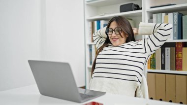 Genç ve güzel İspanyol öğrenci kütüphanede elleri başlarının üzerinde dizüstü bilgisayar kullanıyor.