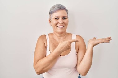 Beyaz arka planda duran orta yaşlı beyaz kadın kameraya hayret ediyor ve gülümsüyor.. 