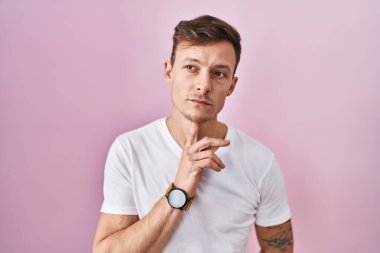 Pembe arka planda duran beyaz bir adam şüphe üzerine yoğunlaşmıştı. Parmakları çenesinde ve yukarı bakıyordu. 