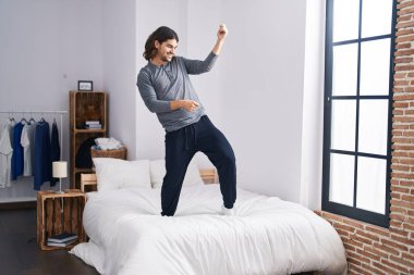 Young hispanic man smiling confident dancing on bed at bedroom