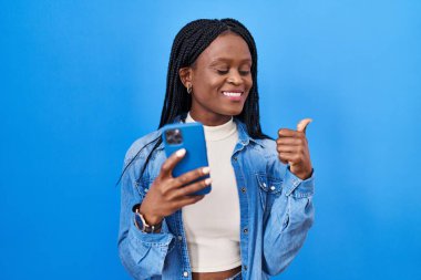 Örgü ören Afrikalı kadın akıllı telefon kullanarak parmak ucunda ağzı açık bir şekilde gülümsüyor. 