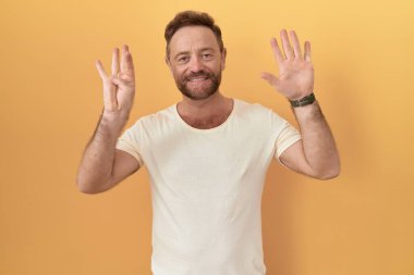 Sarı arka planda duran orta yaşlı bir adam dokuz numaralı parmaklarıyla işaret ederken kendinden emin ve mutlu gülümsüyor.. 