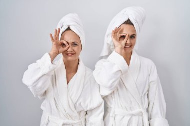 Orta yaşlı kadın ve kız beyaz bornoz ve havlu giyip el hareketleriyle gülümsüyor, gözleriyle mutlu yüzle parmaklarının arasından bakıyor.. 