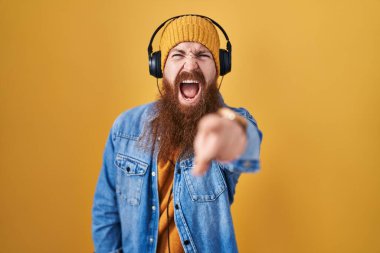 Uzun sakallı, müzik dinleyen beyaz bir adam. Kulaklıkla kameraya rahatsız edici ve hayal kırıklığına uğramış bir şekilde bakıyor. 