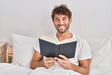 Yatak odasında kitap okuyan genç bir adam.