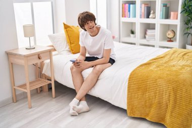 Genç sarışın adam yatakta akıllı telefon kullanıyor.