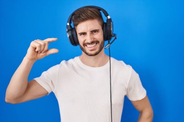 Sakallı, müzik dinleyen, kulaklık takan, gülümseyen, kendine güvenen, el hareketi yapan, parmaklarıyla işaret yapan, kameraya bakan İspanyol bir adam. ölçüm kavramı. 