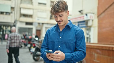 Genç İspanyol adam sokakta gülümseyen akıllı telefon kullanıyor.