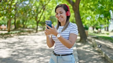 Ortadoğulu kadın parkta kulaklık takıyor.