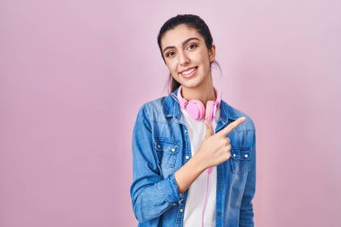 Genç ve güzel bir kadın pembe arka planda neşeli bir şekilde ayakta duruyor. Yüzünde mutlu ve doğal bir ifadeyle elleri ve parmaklarıyla gülümsüyor. 