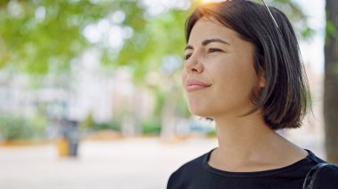Genç, güzel, İspanyol bir kadın parkta ciddi bir ifadeyle yan tarafa bakıyor.