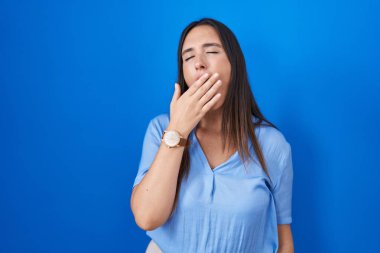 Mavi arka planda duran esmer, genç bir kadın ağzıyla ağzını kapatmaktan sıkılmış. Huzursuz ve uykulu.. 