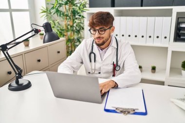 Young arab man wearing doctor uniform using laptop working at clinic