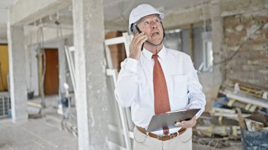 Kıdemli gri saçlı mimar akıllı telefondan konuşuyor. İnşaat alanına bakıyor.