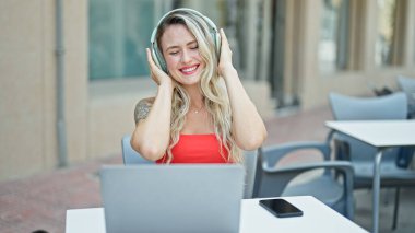 Müzik dinleyen ve dans eden genç sarışın kadın kahve dükkanının terasında oturuyor.