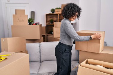 Young beautiful hispanic woman smiling confident holding package at new home