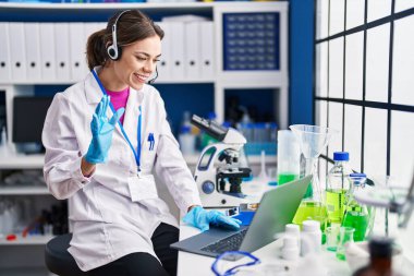 Laboratuvarda çalışan İspanyol kadın pozitif ve mutlu görünüyor. Dişlerini gösteren bir gülümsemeyle ayakta duruyor ve gülümsüyor. 