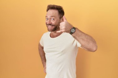 Sarı arka planda duran sakallı orta yaşlı bir adam telefonla el ve parmaklarıyla telefonla konuşuyor gibi gülümsüyor. iletişim kavramları. 