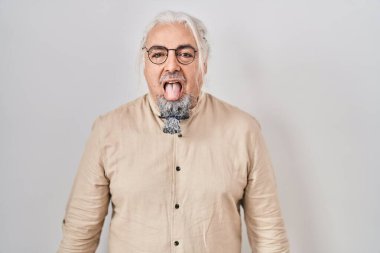 İzole edilmiş arka planda gri saçlı orta yaşlı bir adam komik bir ifadeyle dilini dışarı çıkartıyor. duygu kavramı. 