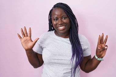 Pembe arka planda duran Afrikalı genç bir kadın 8 numarayı gösterip işaret ederken kendinden emin ve mutlu bir şekilde gülümsüyor.. 