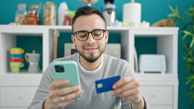 İspanyol adam yemek odasında akıllı telefonuyla online alışveriş yapıyor.