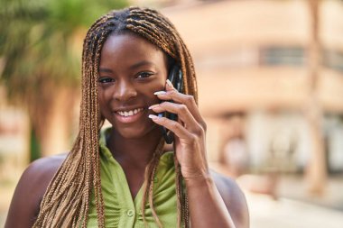 Afro-Amerikalı kadın gülümsüyor. Akıllı telefondan konuşuyor.