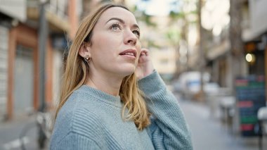 Genç sarışın kadın gökyüzüne bakıyor. Sokakta rahat bir ifadeyle.