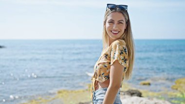 Young blonde woman smiling confident standing at seaside