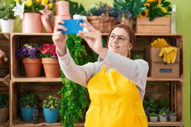 Genç, güzel, kilolu kadın çiçekçi çiçekçide akıllı telefondan selfie çekiyor.