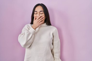 Pembe arka planda duran genç Güney Asyalı kadın ağzıyla ağzını kapatmaktan sıkılmış. Huzursuz ve uykulu.. 