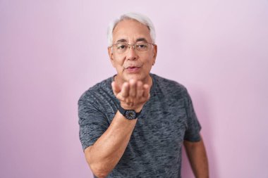 Pembe arka planda gri saçlı, orta yaşlı bir adam kameraya bakıp havada öpücükler savuruyor. Güzel ve seksi. aşk ifadesi. 