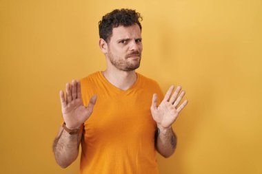 İspanyol genç adam sarı arka planda duruyor. Avuçlarını hareket ettiriyor. Korkmuş ve iğrenç bir ifadeyle reddediyor. Dur ve yasakla. 