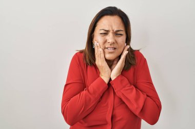 Beyaz arka planda dikilen Latin kökenli olgun bir kadın diş ağrısı ya da diş ağrısı yüzünden elleriyle dudaklarına dokunuyor. dişçi 