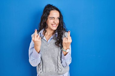 Young brunette woman standing over blue background showing middle finger doing fuck you bad expression, provocation and rude attitude. screaming excited 