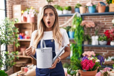 Young blonde woman working at florist shop afraid and shocked with surprise and amazed expression, fear and excited face. 