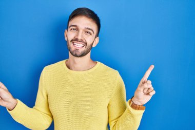 Mavi arka planda duran İspanyol adam parmaklarıyla farklı yönleri işaret ederek gülümsüyor. reklam için kopyalama alanı 