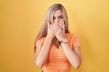 Sarı arka planda duran genç bir kadın ağzını yanlışlıkla ellerle kapatarak şok etti. gizli kavram. 