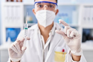 Tıbbi maske takan genç İspanyol bilim adamı laboratuarda kovid aşısı tutuyor.