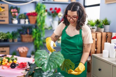 Çiçekçide çiçekçiye sprey sıktığından emin bir şekilde gülümseyen genç kadın.