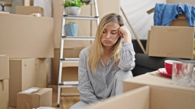 Genç sarışın kadın yeni evinde stresli bir ifadeyle yerde oturuyor.