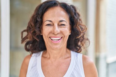 Orta yaşlı bir kadın sokakta kendine güvenerek gülümsüyor.