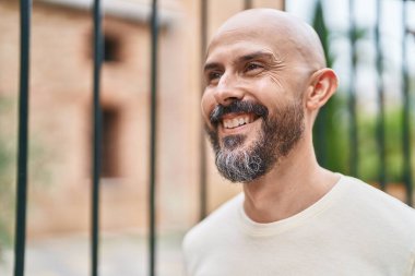 Genç kel adam gülümsüyor. Kendinden emin bir şekilde caddeye bakıyor.