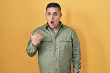 Sarı arka planda dikilen İspanyol genç adam elleri yana doğru işaret ederek şaşırdı, ağzı açık hayret içinde kaldı.. 