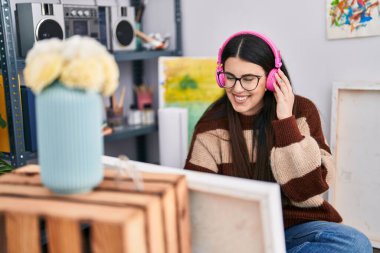 Young hispanic woman artist listening to music drawing at art studio