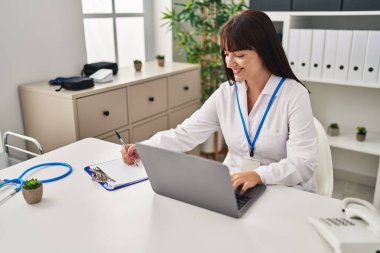 Genç, güzel İspanyol kadın doktor klinikteki belgelerde dizüstü bilgisayar kullanıyor.