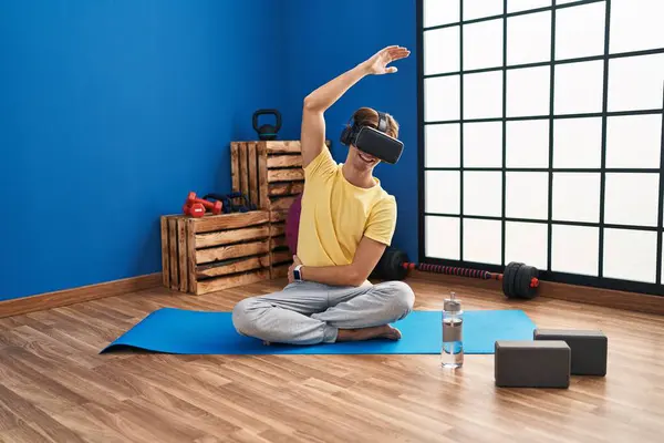 Young caucasian man using virtual reality glasses stretching at sport center