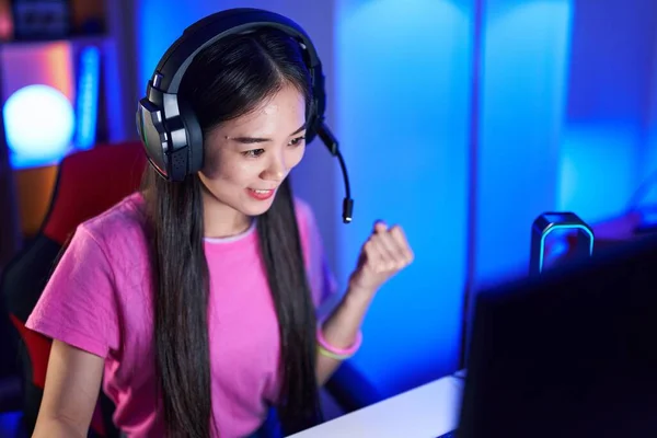 Young chinese woman streamer playing video game with winner expression at gaming room