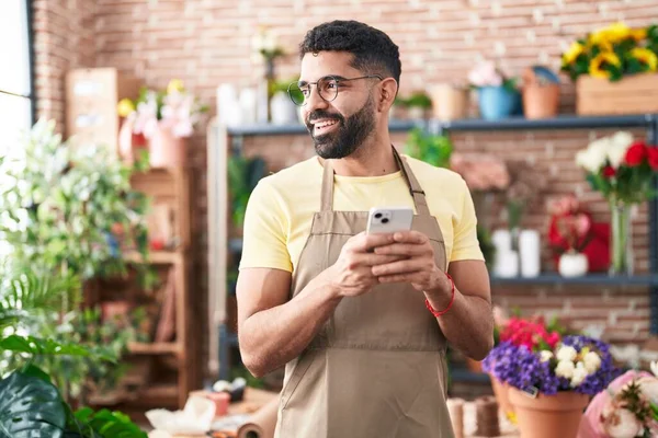 Young arab man florist smiling confident using smartphone at florist